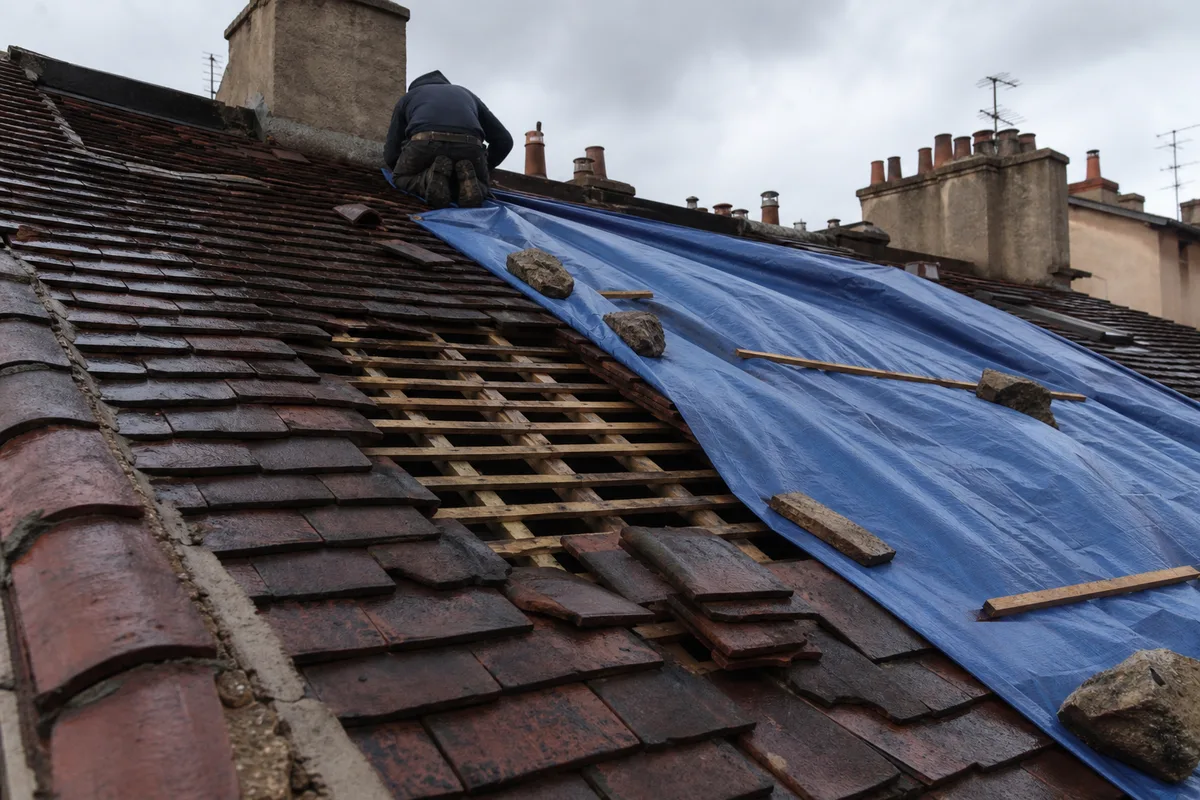 Toiture d’un immeuble ancien lyonnais après un coup de vent, quelques tuiles déplacées et un bâchage provisoire tendu sur la pente