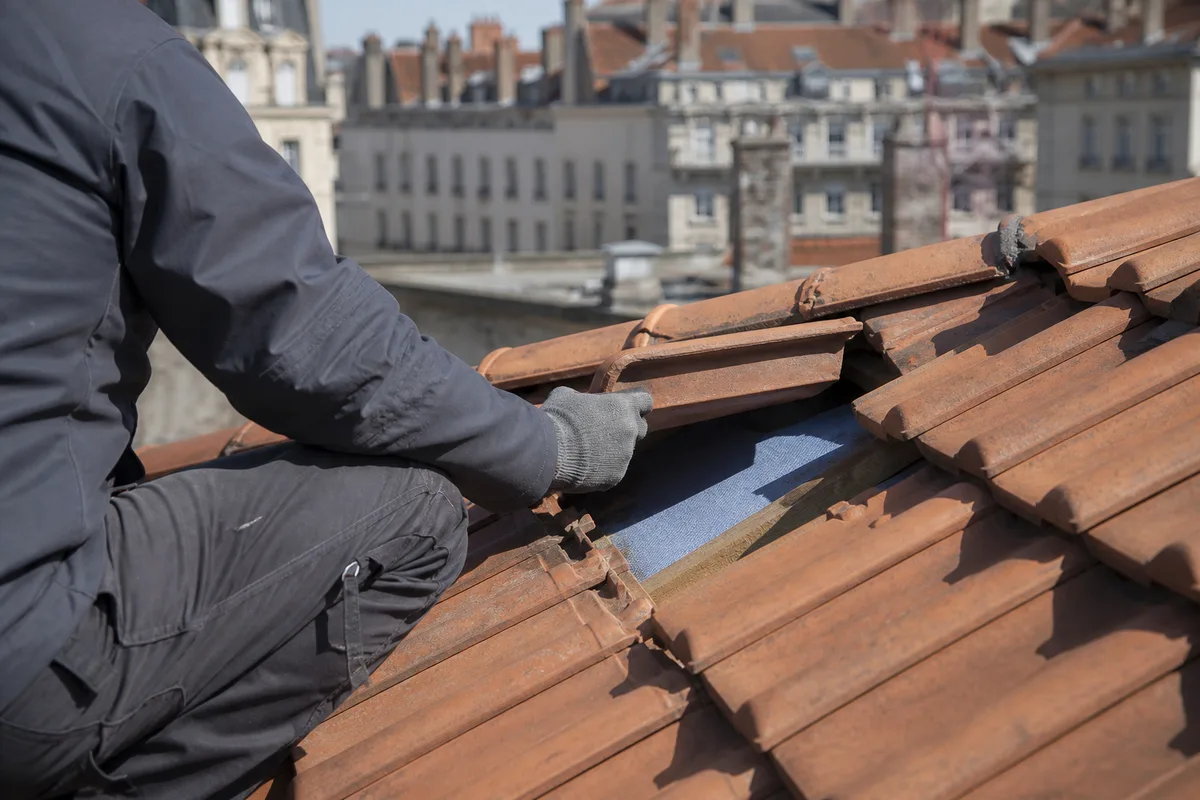 Couvreur inspectant une toiture en tuiles mécaniques d’un immeuble ancien lyonnais sous une lumière claire